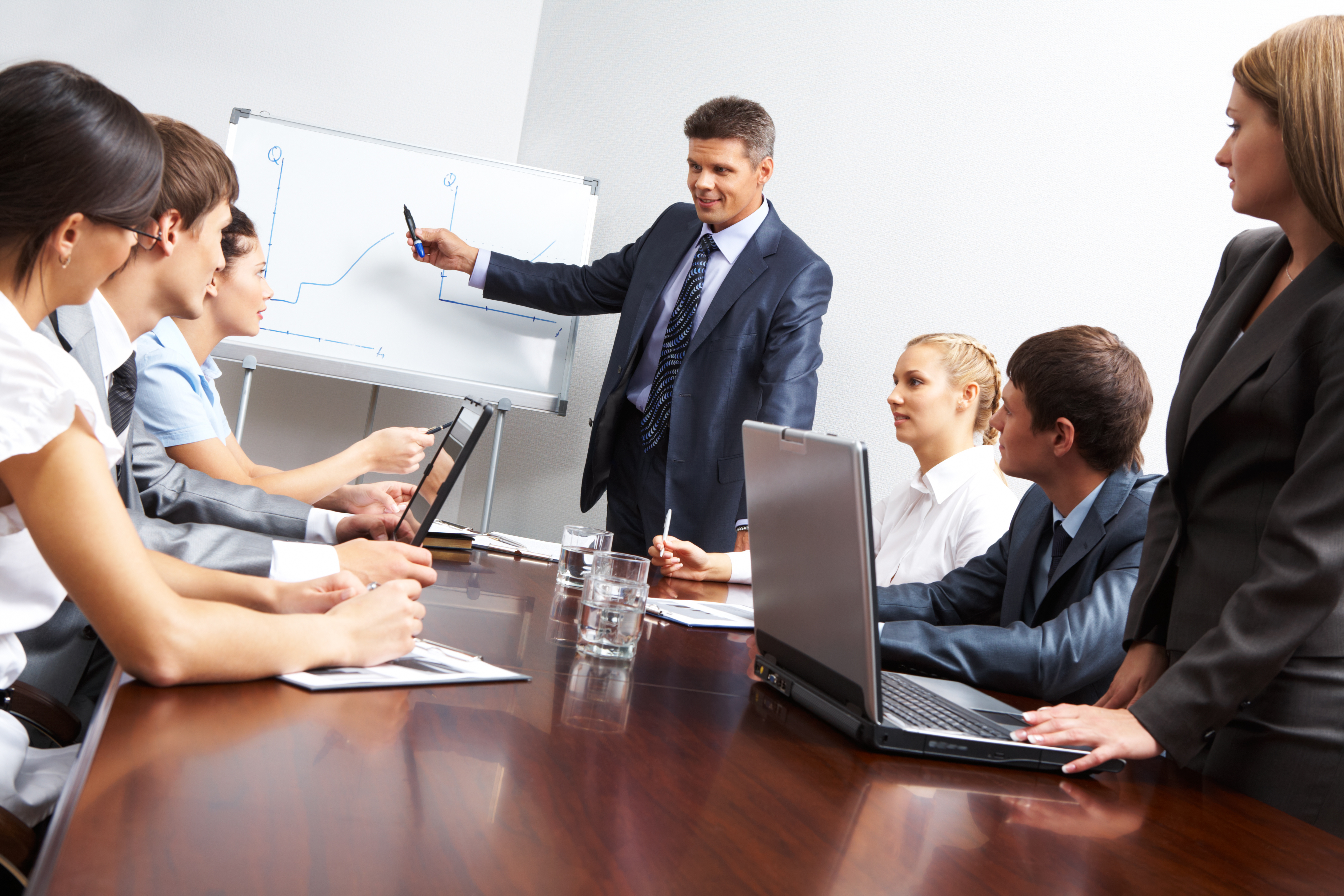 Image of smart business people looking at their leader while he explaining something on whiteboard during seminar